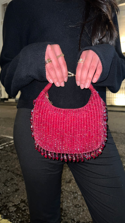 Person holding a pink beaded handbag with a blurred background